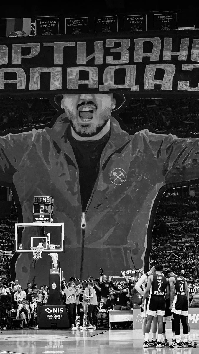 Black and white photo of a giant tifo banner covering a whole stand above the court during a timeout